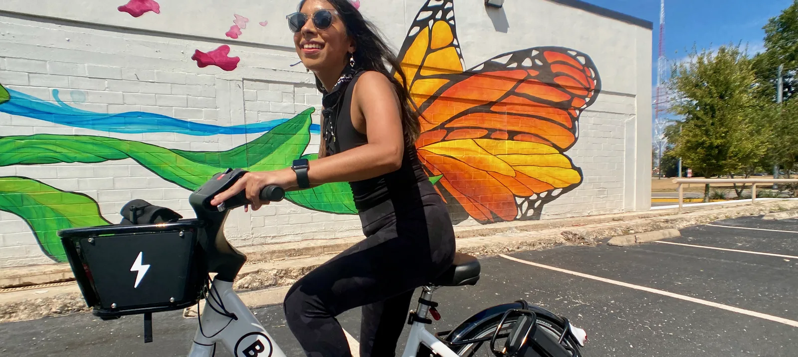 Latina woman riding a bike share bicycle in front of a butterfly mural