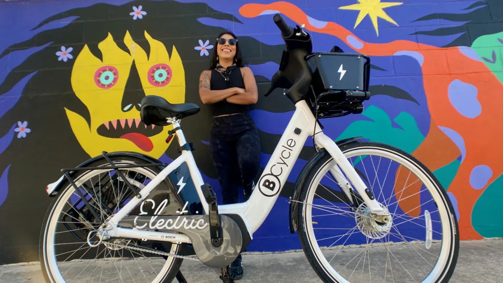 Latina woman leaning on a mural with a bike share bicycle